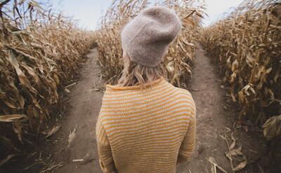 Exploring a corn maze, a woman in an autumn-hued sweater reflects the serene beauty of fall.