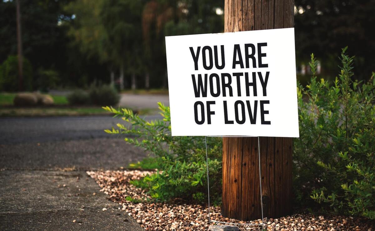 You are worthy of love sign beside tree and road.