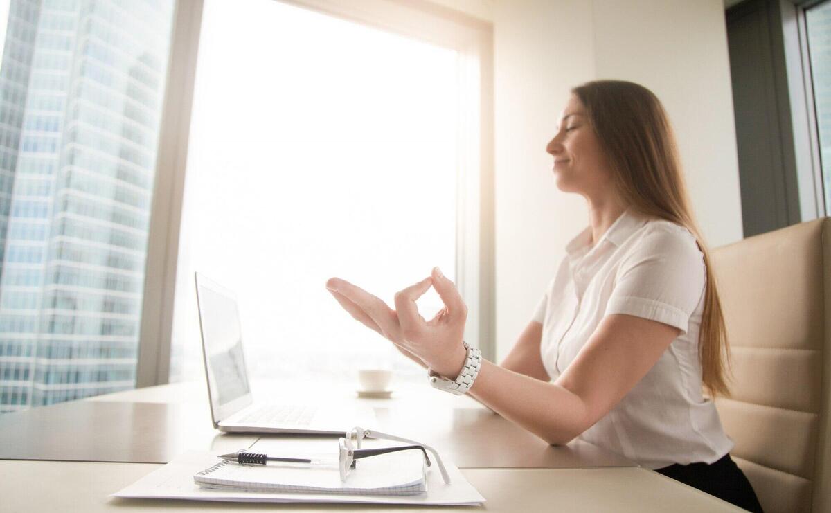 Calm peaceful businesswoman practicing yoga at work, meditating in office