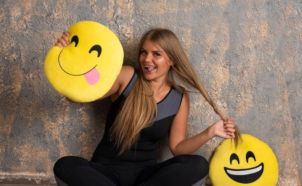 Young sportive girl in sport outfits holding a smiling and tongue out emoji pillows and having fun.