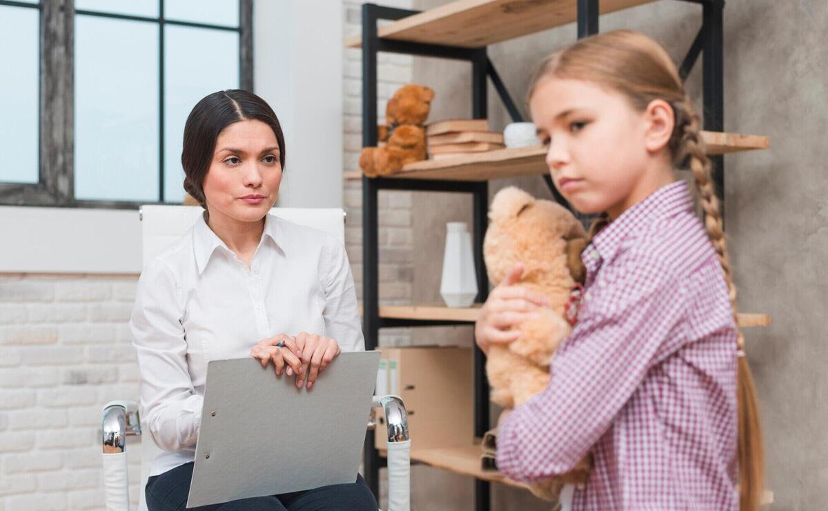 Female psychologist having a therapy session with sad girl holding teddybear in hand