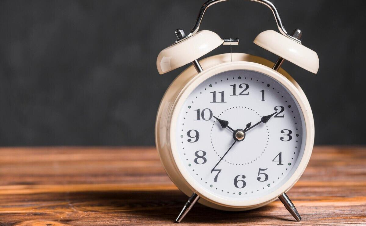 An old vintage alarm clock on wooden desk against black background