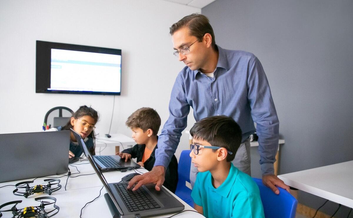 Pupils doing task on laptops and focused teacher monitoring them