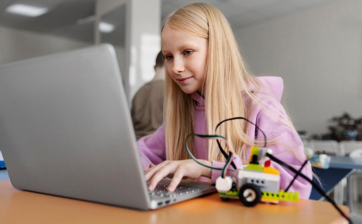 Young girl using a laptop and electronic parts to build a robot