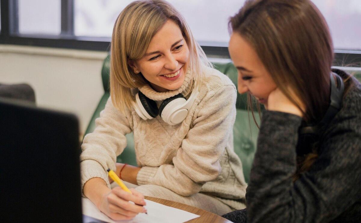 Smiling females wearing headphones around the neck looking at laptop