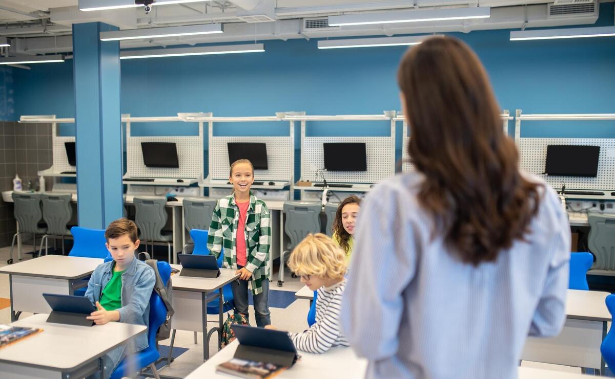 Woman looking at girl answering standing near desk