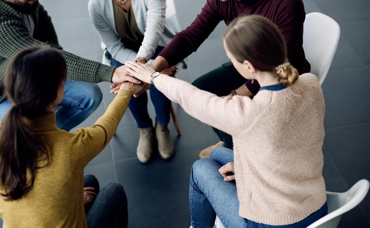 Participants of group therapy gathering hands in unity during a session at medical center