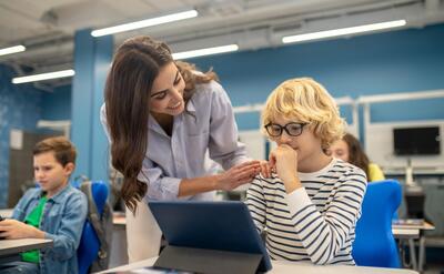 Smiling teacher touching shoulder of boy looking at tablet