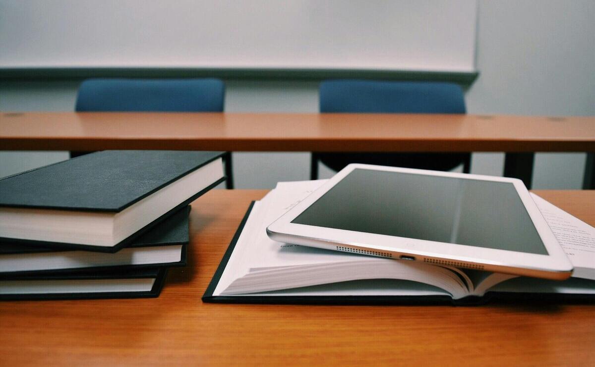 Books and a tablet on a desk in a classroom, depicting modern education.