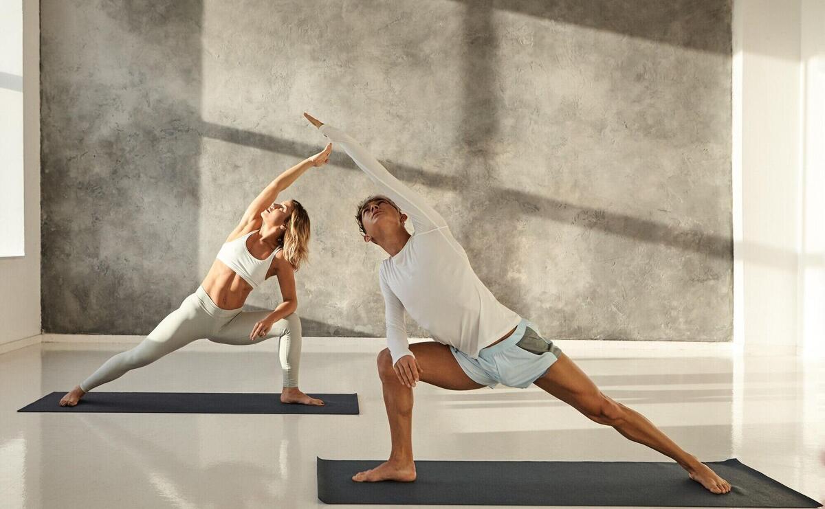 Young couple practicing yoga together. Indoor picture of handsome tanned guy on mat doing standing pose s to strengthen legs, stretching arms and looking up