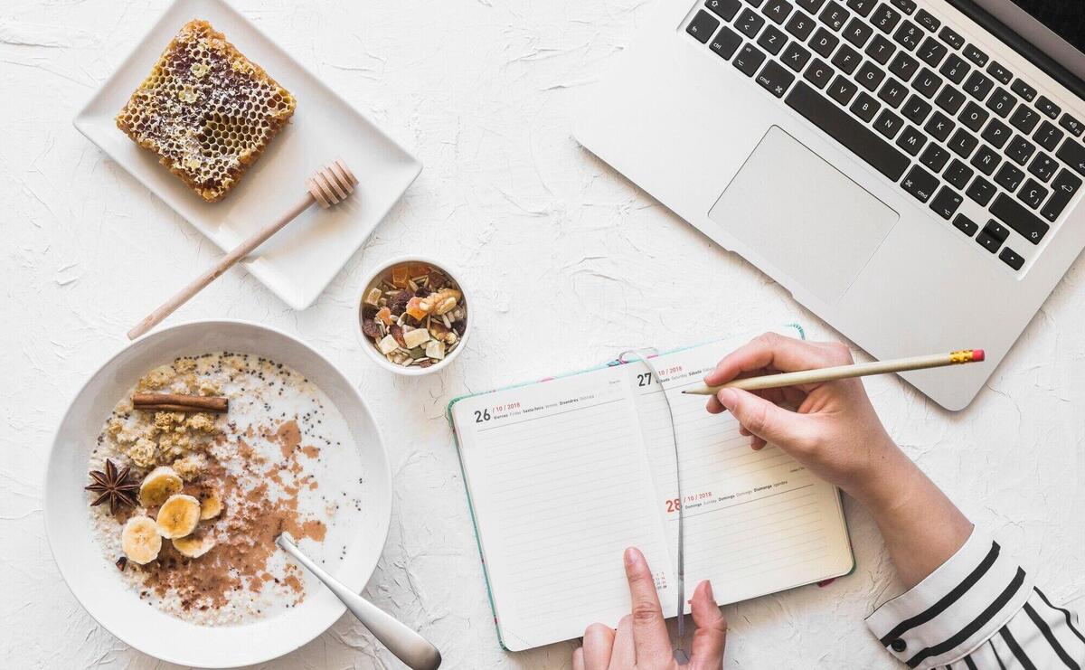 Businesswoman writing diary with pencil on workplace with laptop and healthy breakfast