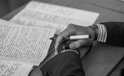 Close-up of a hand holding a pen over pages of writing on a desk.