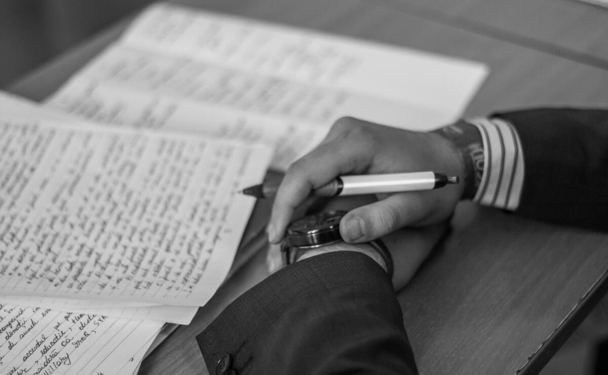 Close-up of a hand holding a pen over pages of writing on a desk.