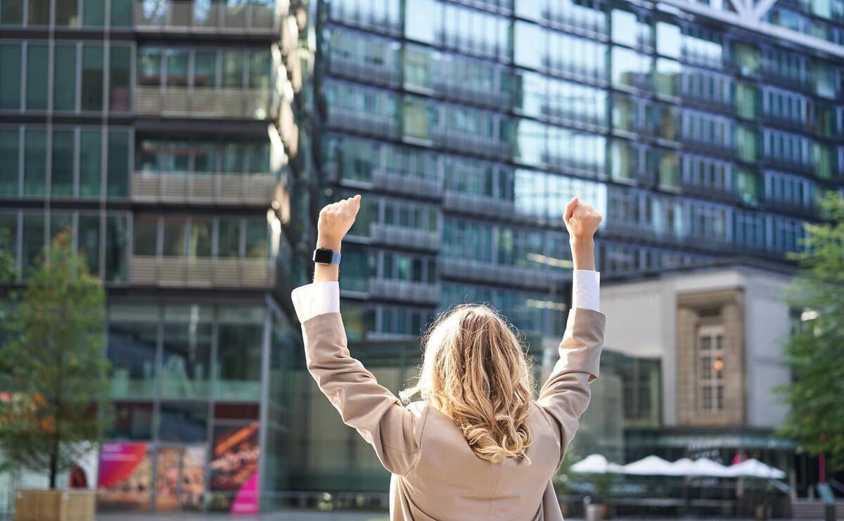 Rear view of corporate woman lawyer celebrating lifting hands up and triumphing achieve goal or succ