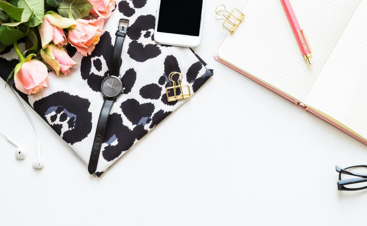 Stylish flat lay of office essentials including pink roses, watch, notebook, and accessories on white background.