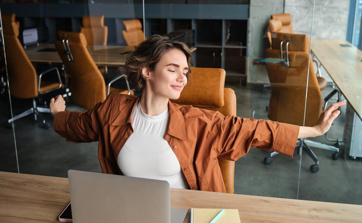 Portrait of woman resting in office stretching arms after sitting and working on laptop