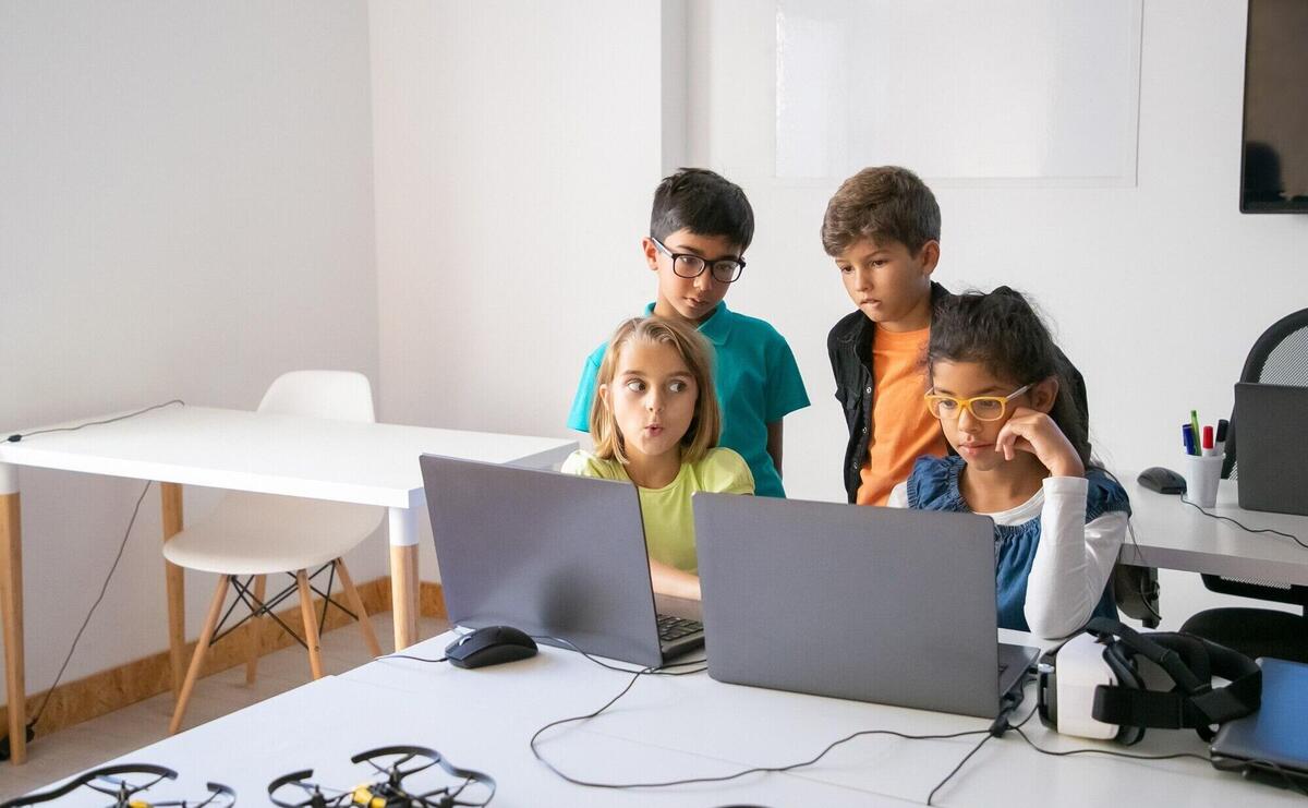 Little classmates doing group task, using laptops and studying at computer school