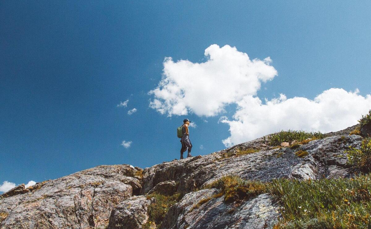 Low angle shot of a male with a backpack standing on the edge of the mountain under cloudy sky