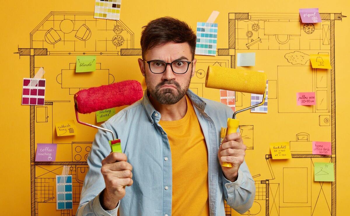 Serious young male stands next to house design sketch ready for renovation