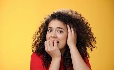 Expressive woman with curly hair showing surprise on yellow background.