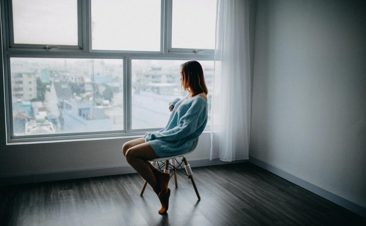 A woman in a sweater gazes out a window, lost in thought.