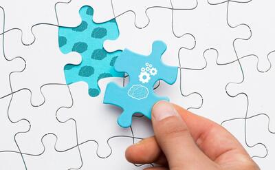 Close-up of human hand holding blue puzzle piece with brain and cogwheel drawing