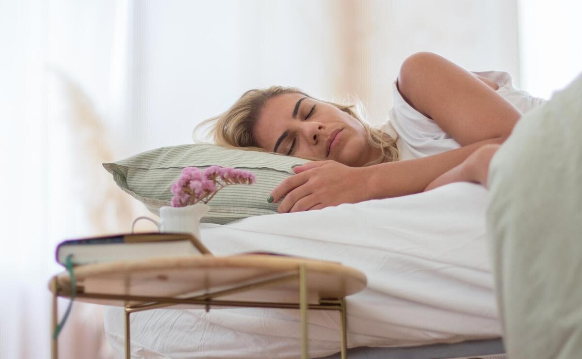 Peaceful woman sleeping in bed under cover in morning. Medium shot of attractive woman lying in bed, relaxing and having rest on weekend, enjoying soft linen. Dream, sleeping concept