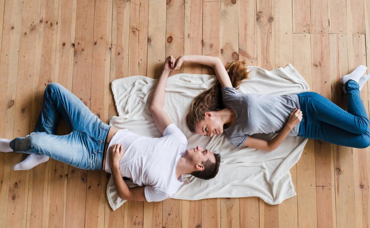 Couple holding hands on sheet on floor.