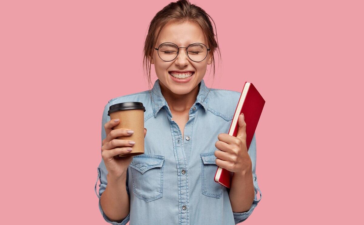 Waist up shot of pretty smiling female recieves pleasure from studying