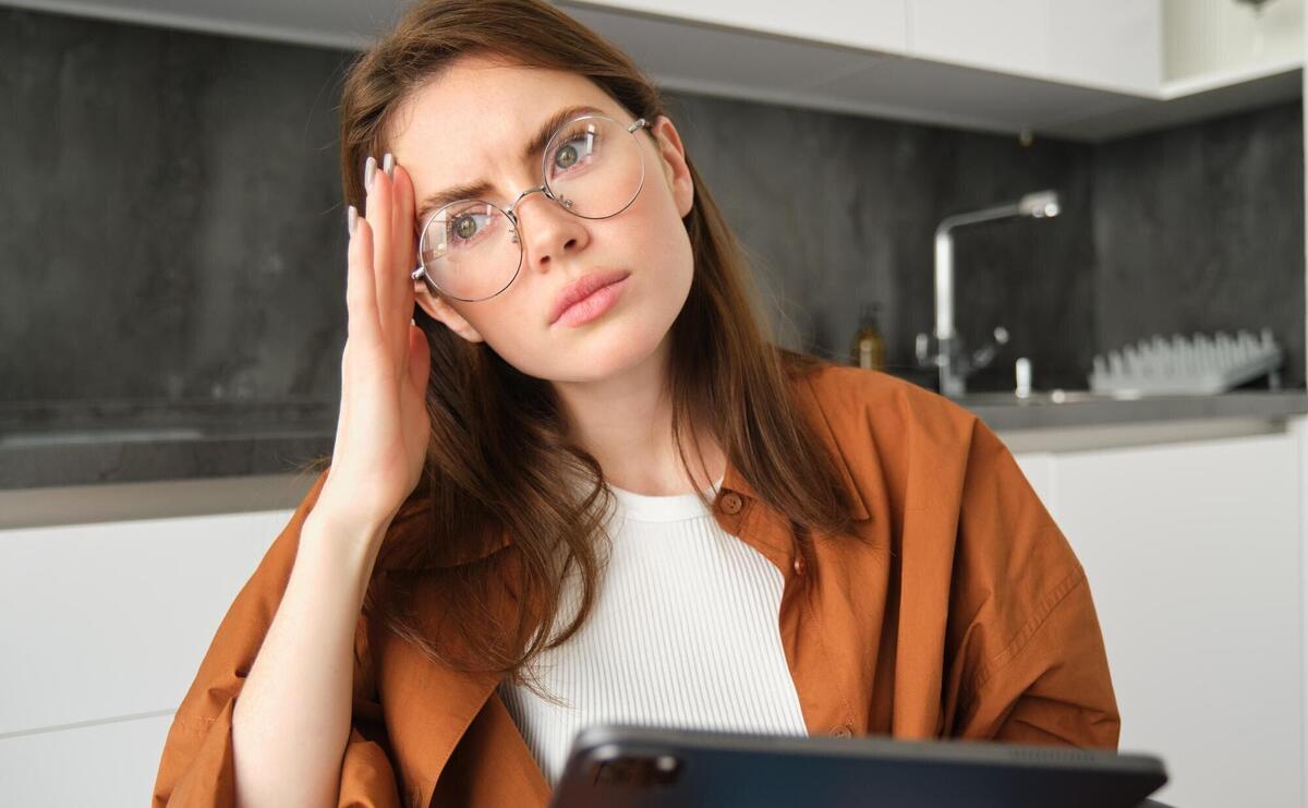 Portrait of brunette woman working from home wearing glasses looking concerned touching head and