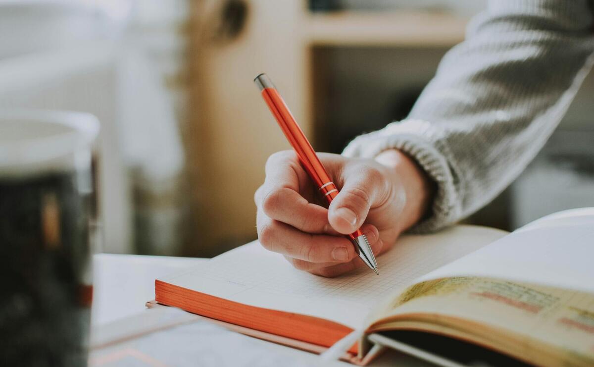 person holding on red pen while writing on book