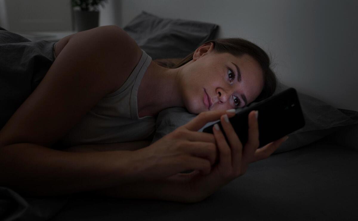 Woman lying in the bed during the night and using a phone.
