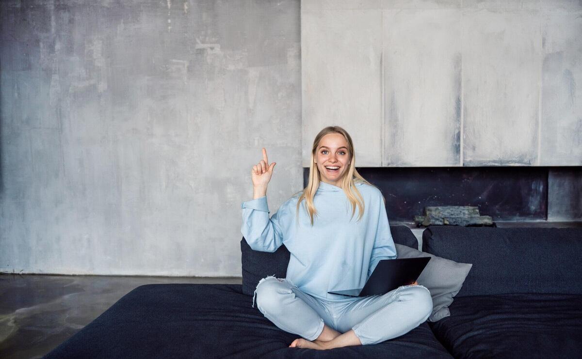 Image of happy woman using silver laptop while sitting on sofa