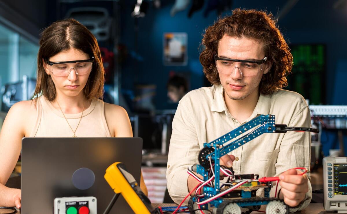 Young man and woman in protective glasses doing experiments in robotics in a laboratory.